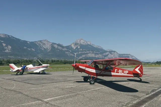 Petits avions d’aéroclub sur un aérodrome, montagnes au fond